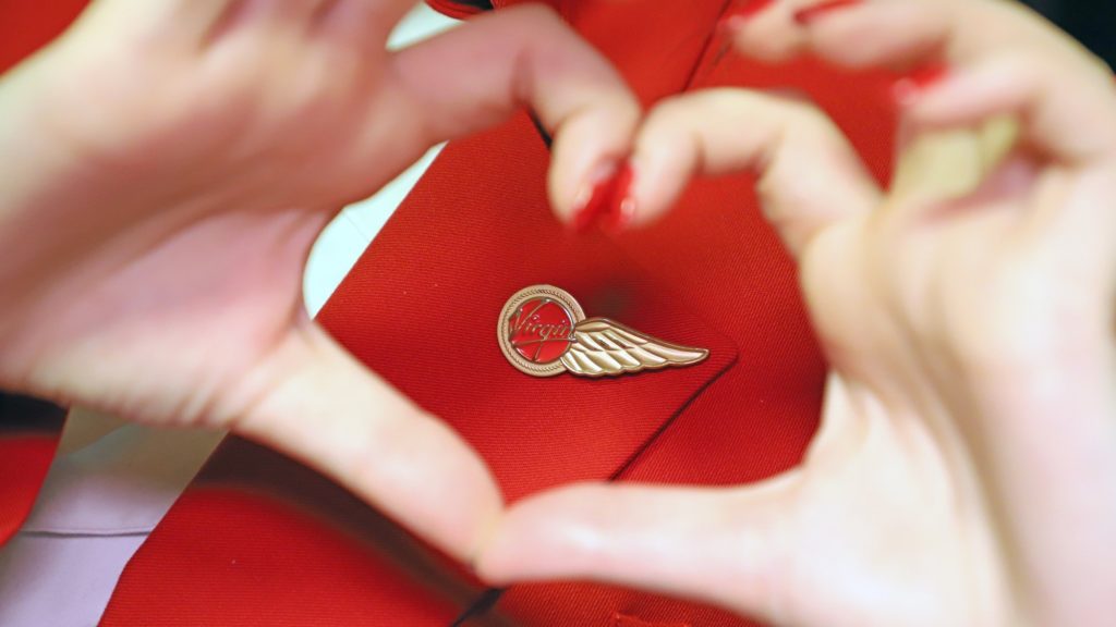 Virgin Atlantic cabin crew making a love hear shape with their hands around their flight attendant wings