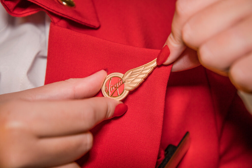 A woman holds a red and white winged badge featuring the Virgin Atlantic logo.